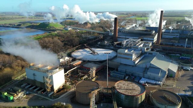 Aerial drone view of large scale industrial factory, sugar beet production processing facility, smoke from chimneys and clarifying tanks for used water cooling, Wissington, United Kingdom.
