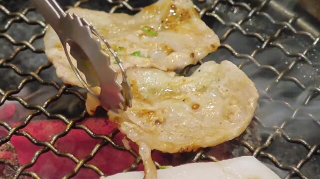 Grilling sliced pork on a barbecue grill, flipping back and forth with smoky and appetizing steam.