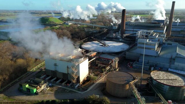 Aerial drone view of large scale industrial factory, sugar beet production processing facility, smoke from chimneys and clarifying tanks for used water cooling, Wissington, United Kingdom.