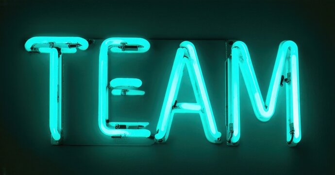 Bright turquoise neon sign spells TEAM against dark background. Simple, modern aesthetic. Bold lettering creates strong visual impact.