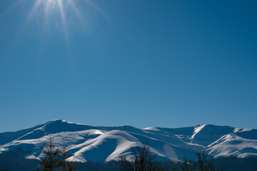 Sunny winter mountain landscape with snow-covered peaks, evergreen forest and clear blue sky, showcasing pristine alpine nature, cold season scenery and peaceful wilderness environment