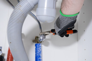 Gloved hand uses a wrench to tighten a water pipe valve under a sink, demonstrating plumbing...