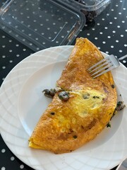 Omelette with mushrooms garnished with herbs on white plate with fork on dotted background