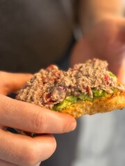 Hands holding tuna and avocado open sandwich with blurred background