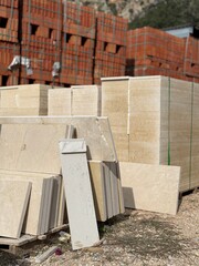 Construction materials stacked outdoors with piles of bricks and stone slabs in the background