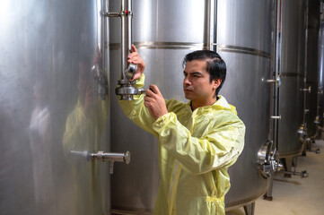 Expertise wine maker man working and inspecting wine from metal fermentation container in fermenting room