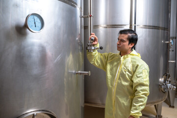 Expertise wine maker man working and inspecting wine from metal fermentation container in fermenting room