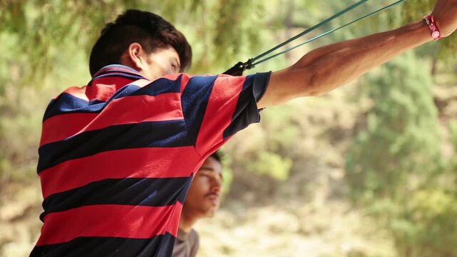 A village boy pulls a slingshot to shoot tree seeds into a forest in Uttarakhand. The scene reflects poverty, childhood creativity, nature care, and rural mountain life.