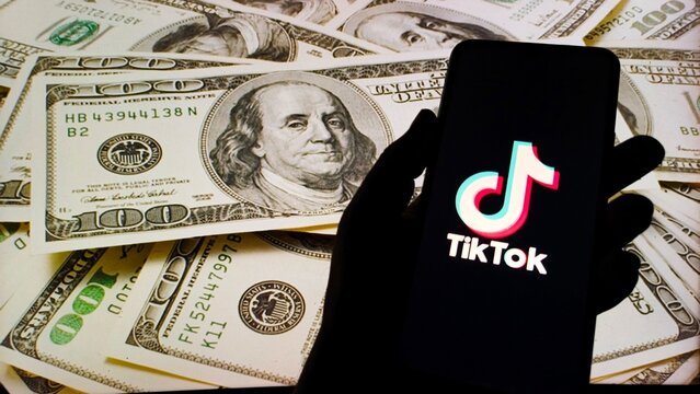 Hand holding smartphone with TikTok logo on screen over US dollar bills