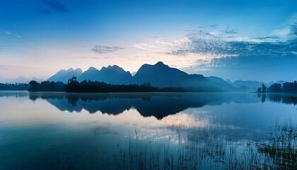 Serene Blue Mountain Landscape Reflection In Calm Water Under Misty Sky At Dawn