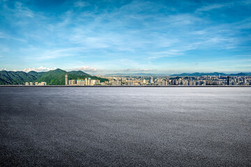 Empty asphalt road with city skyline and mountain background.