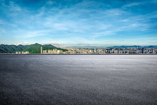 Empty asphalt road with city skyline and mountain background.