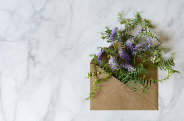 Florist at work: a pretty woman prepares a summer bouquet of white gypsophila on a gray desk. Kraft paper, scissors, greeting envelope on the table. View from above. The composition is flat.