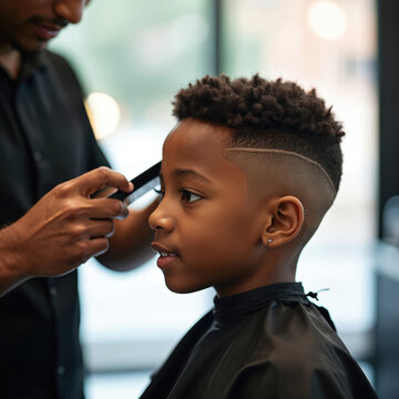Young african american boy gets trendy fade haircut at modern barber shop. Barber uses comb for styling curly dark hair. Child sits under cape during grooming session.