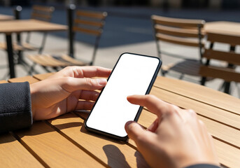 Person's hands holding and touching a blank screen smartphone at an outdoor cafe table