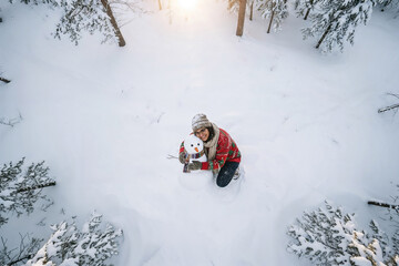 Ragazza di origini indiane vestita con un maglione rosso, guanti, berretto e sciarpa gioca con un pupazzo di neve in inverno