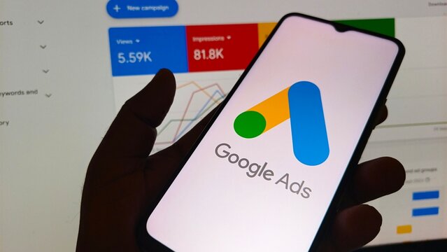 Hand holding smartphone with Google Ads on screen showing analytics dashboard