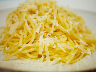 Closeup view of cooked spaghetti covered with grated parmesan cheese on a white plate, warm cheesy pasta portion for Italian comfort food and restaurant menu visuals
