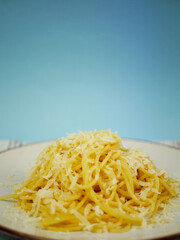 Plate of spaghetti with grated parmesan cheese on blue and white background, vertical Italian pasta image for restaurant posters, menus and social media content
