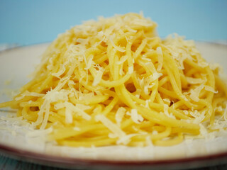 Side closeup of hot spaghetti piled high and topped with grated parmesan cheese on a plate, appetizing cheesy pasta portion for Italian comfort food concepts