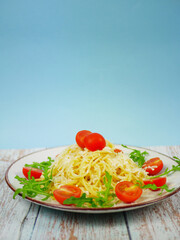 Plate of spaghetti with parmesan, arugula and cherry tomatoes standing on rustic wooden surface against blue background, Italian pasta salad with copy space for design