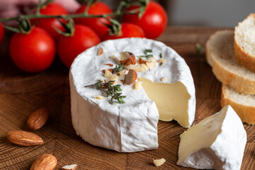 Cheese platter with brie or camembert cheese served with chopped almonds and baguette slices on wooden board