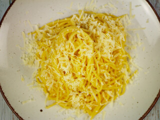 Close top view of cooked spaghetti generously sprinkled with grated parmesan cheese on white plate, detailed cheesy pasta texture for Italian food backgrounds and designs