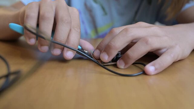 Child repairing small electronic device at table using screwdriver and tools. Hands-on learning, technology curiosity and home electronics repair concept in indoor setting
