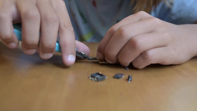 Child repairing small electronic device at table using screwdriver and tools. Hands-on learning, technology curiosity and home electronics repair concept in indoor setting