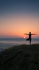 Fototapeta premium Woman practicing yoga at sunrise on hill, surrounded by misty landscapes, creating serene and peaceful atmosphere