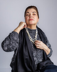 Woman adjusting a layered pearl necklace while posing confidently against a neutral background.