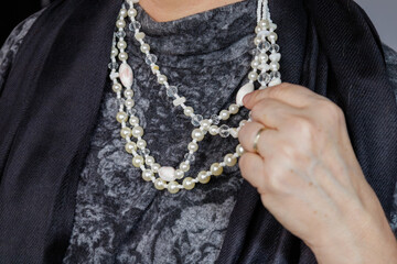 Close-up of a layered pearl necklace held by a hand against textured fabric.
