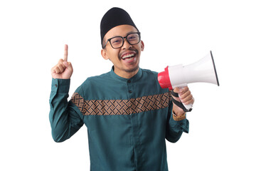 Excited Asian Muslim man in a green traditional outfit pointing at empty copy space while holding a...