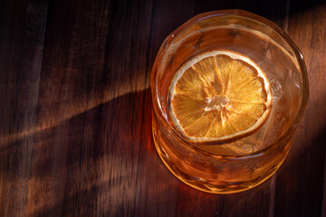 whiskey cocktail served on the rocks garnished with a dehydrated orange slice with dramatic lighting served on a wooden surface.