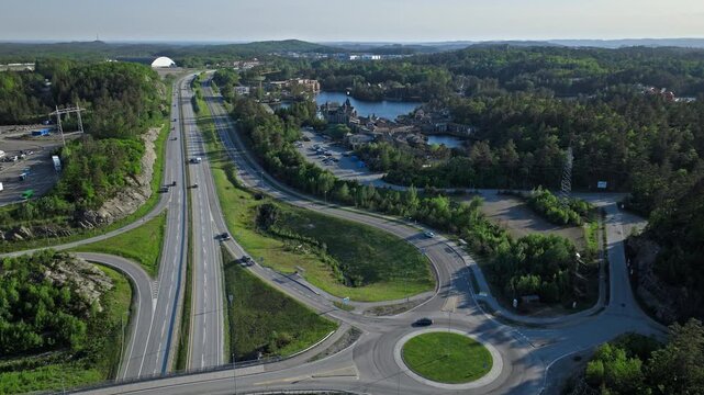 Aerial view of Norwegian highway.. Drone panorama shows the E18 road, roundabout, forest landscape, and Abra Havn pirate village at Dyreparken on a sunny summer day.