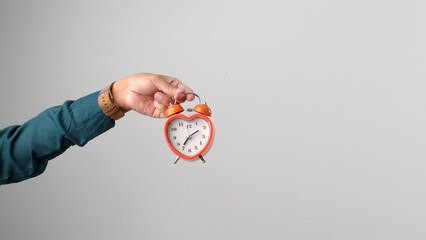 Hand holding an orange, heart-shaped alarm clock. Isolated on white background. Concept of time, love, schedule, or romantic timing