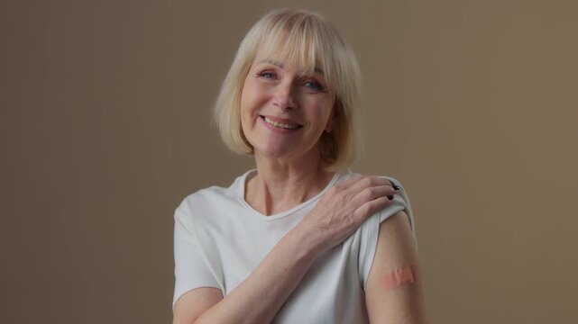 Portrait in studio old Caucasian woman showing adhesive medical plaster looking at camera senior female retired granny recommend coronavirus vaccination immunization covid19 injection medicine health