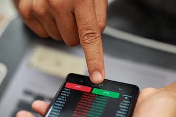 Close up of a person's hand holding a smartphone displaying stock market data with currency symbols