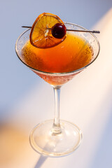 Beautiful amber cocktail, a Negroni or manhattan served up on a white surface with dramatic lighting.