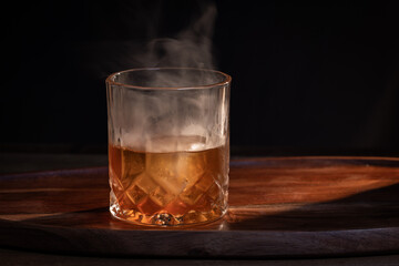 Smoked whiskey cocktail served on the rocks with dramatic lighting served on a wooden surface.
