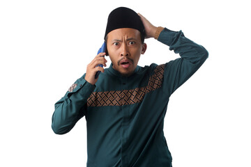 Surprised Asian Muslim man in a green traditional outfit listening on a phone call with a raised eyebrow and shocked expression, Isolated on a white background. Concept of unexpected news, disbelief