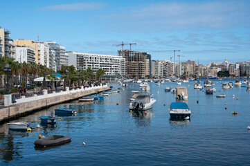 Blue coastline of Il-Gżira with high apartment blocks, small boats and a busy bay, capturing a lively and slightly chaotic Mediterranean holiday atmosphere Il-Gżira, Malta, 9 DEC 2025.