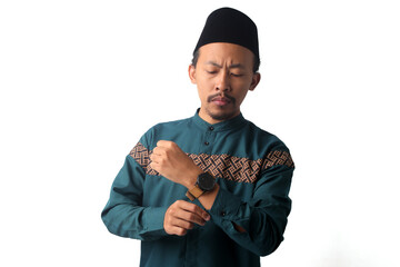 Young Asian Muslim man wearing traditional Indonesian attire, a baju koko and black peci (songkok), and a wristwatch during Ramadan. Isolated on a white background