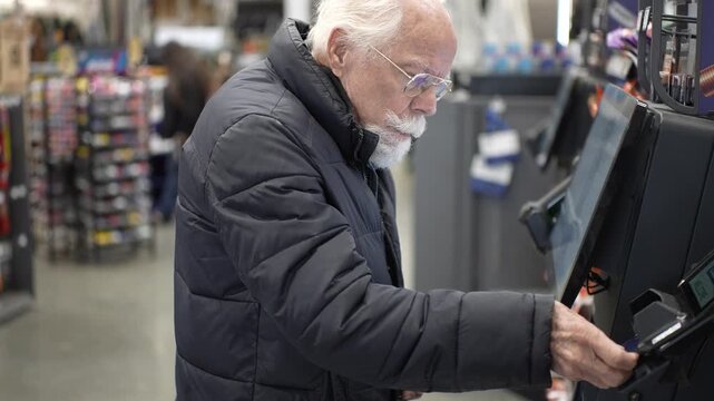 Senior man shops at a hardware store and interacts with self checkout machines. He scans items and completes his purchase.