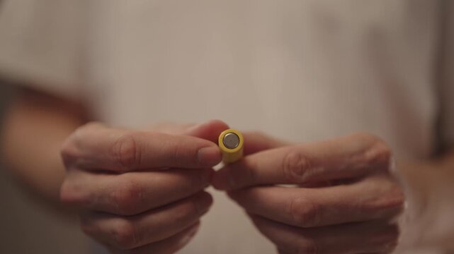 Close-up of person holding two battery, examining yellow aa size battery before installing into electronic device, symbolizing power, energy, renewal of electrical charge for technology applications.