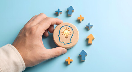 hand holding wooden token with lightbulb head profile and growth symbols
