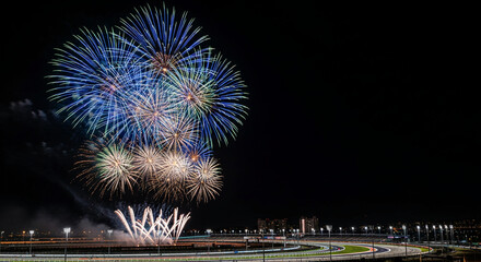 Vibrant blue and white fireworks light the night sky over a racetrack, representing celebration, event, or festive occasion against a black background