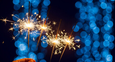Several sparklers emit bright, radiant light against a backdrop of diffused blue orbs, representing celebration, festivity, and exciting event or occasion