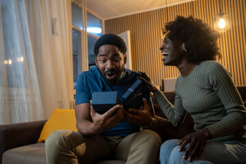 Obraz premium Black couple exchanging gifts, man thrilled, smiling as woman hands present