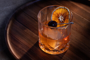 whiskey cocktail served on the rocks garnished with a dehydrated orange slice with dramatic lighting served on a wooden surface.
